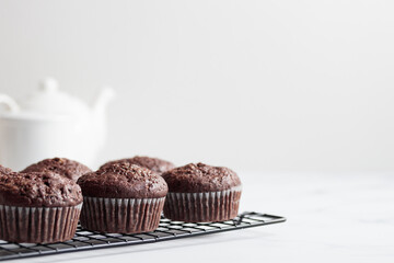 Freshly baked chocolate muffins on a grid on white table
