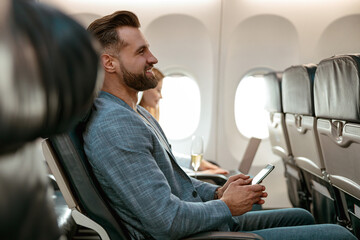 Cheerful bearded man using smartphone in airplane