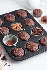 Freshly baked chocolate muffins in a baking pan on white table with ingredients