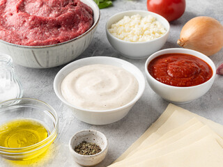 Lasagna ingredients top view. Ground beef (minced), mozzarella cheese, tomato sauce, bechamel sauce, olive oil, onion bulb, garlic cloves,basil. Traditional italian dish. Grey concrete background.