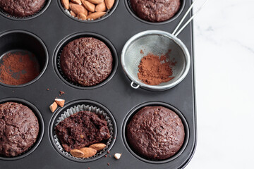 Freshly baked chocolate muffins in a baking pan on white table with ingredients