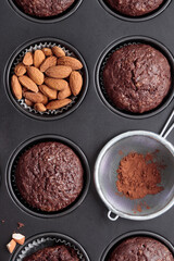 Freshly baked chocolate muffins in a baking pan on white table with ingredients