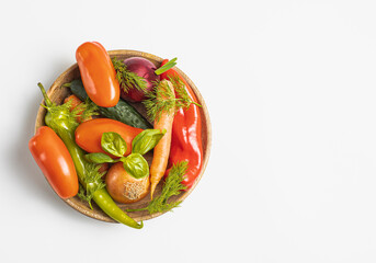 Traditional wooden plate with fresh seasonal vegetables: green pepper, tomato, onion, carrot, cucumber, basil, dill on white background, space for a text,  top view, stock photo