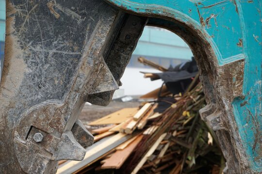 Alte abgerissene Holzlatten zwischen blauer Baggerzange aus Stahl 
