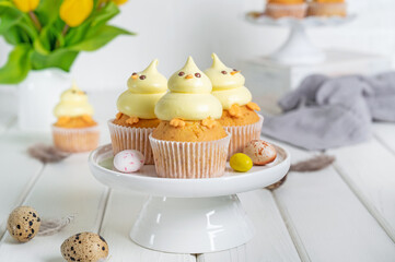 Cute Easter chick cupcakes. Vanilla cupcakes with buttercream on a white stand with fresh flowers on a white wooden background. Copy space.