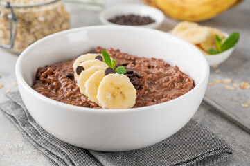 Chocolate oatmeal porridge with banana and chocolate chips on top in a white bowl. Healthy...