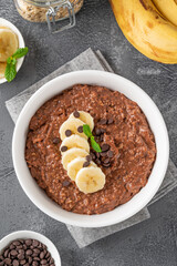 Chocolate oatmeal porridge with banana and chocolate chips on top in a white bowl. Healthy breakfast. Copy space.