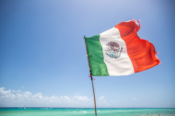 Mexican flag partially ripped by the wind blowing from the turquiose Carribean Sea