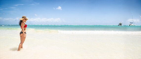 Banner of a woman in hat, sunglasses and swimsuit standing in the shallow sea with boats on the horizon, enjoying great summer holiday weather