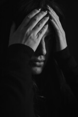 Black and white portrait of a beautiful young woman who tries to hide her face with her hands and go unnoticed