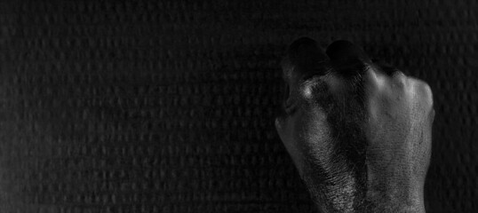 A clenched male hand that had been painted with black paint. Dark, textured background.
