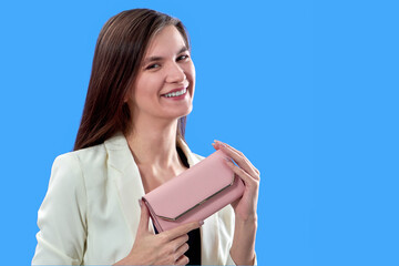 Obraz premium A beautiful young woman is holding a pink purse on a blue background, copy space