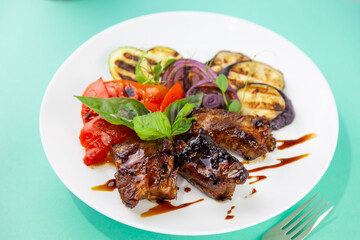 Grilled meat and vegetables. Zucchini, peppers, red onions and basil. Fried pork medallions. Food on a white plate in a restaurant