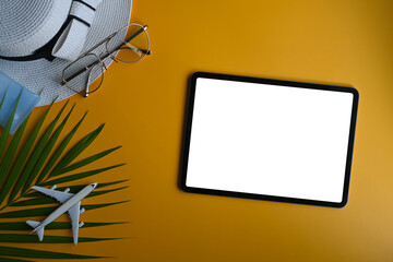 Top view digital tablet, traveler accessories and palm leaves on yellow background. Travel, summer and holiday concept.