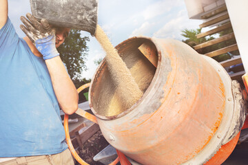 Man adds sand from bucket into cement mixer at DIY construction