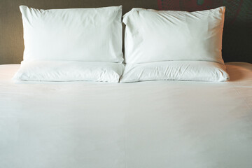 Clean Bedding sheets and pillow on natural wall room background. White bedding and pillow in hotel room. White pillows on empty bed.