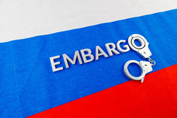 the word embargo laid with silver metal letters on russian tricolor flag with silver handcuffs