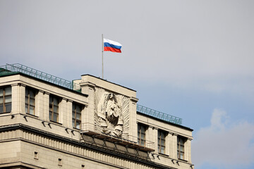 Russian flag on the parliament building in Moscow on background of blue sky and white clouds, authorities of Russia