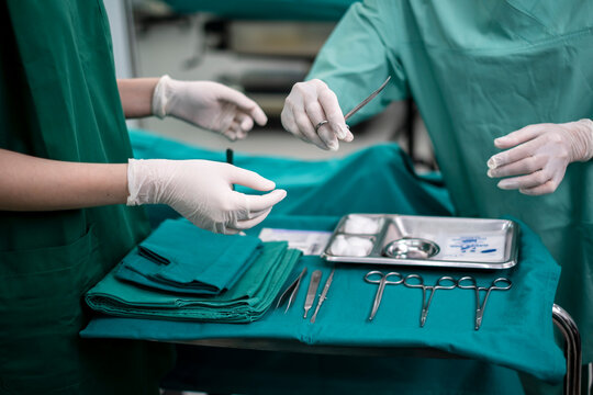 Professional Medical Surgeons team performing surgical operation. Surgical operation. Surgeons at work in operating theater toned in green. Nurse preparing medical tools for operation.