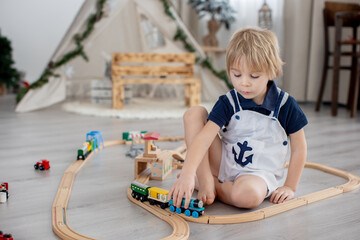 Cute blond toddler child, boy, playing with colorful trains and railroad at home