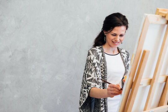 beautiful woman artist paints a picture with paints on an easel