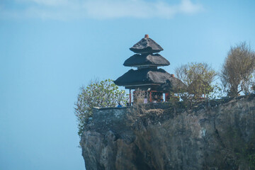 Fototapeta premium A view on Uluwatu Cliffs, Bali, Indonesia. There is a small temple on the top of the cliff. The waves are rushing to the shore, making the water bubbly. Steep and dangerous fall. Hidden gem