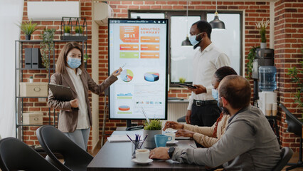 Business people doing teamwork for project planning and presentation. Colleagues with face mask working on startup development and marketing strategy with monitor during pandemic.