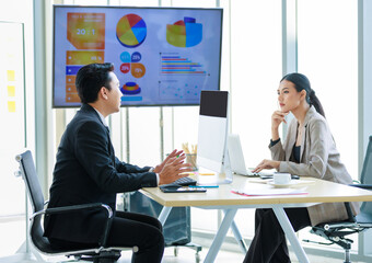 Asian professional successful businessman and businesswoman employee in formal suit sitting at working desk in meeting room discussing brainstorming together about company growth target and margin