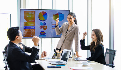 Happy excited cheerful Asian professional successful businessman businesswoman team colleagues in formal suit sitting standing in meeting room holding fists up celebrating job achievement together