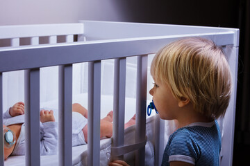 Toddler boy brother look in the crib of newborn sister