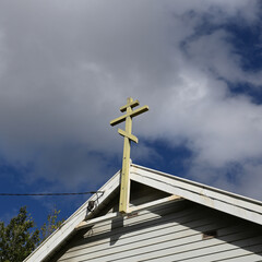 Simple wooden Eastern Orthodox Cross, or Russian Orthodox Cross, affixed atop a white weatherboard...