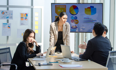 Asian stressed depressed upset female businesswoman employee in formal suit sitting holding hand touch head having migraine headache while other colleagues talking discussing together in meeting room