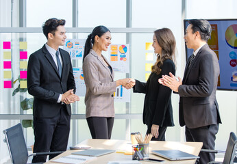 Asian young happy professional successful businessman and businesswoman partnership standing shaking hands greeting together while having job agreement achievement deal done in company meeting room