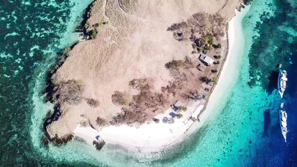 Top down drone shot of paradise island in Komodo National Park, Flores, Indonesia. The island has scarcely any plants and is surrounded with idyllic white sand beaches. Few boats anchored on the shore