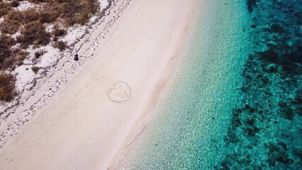 A drone shot of a heart drawn on the sand a small island near Maumere, Indonesia. Happy and careless moments. Waves gently washing the shore. Romance and love