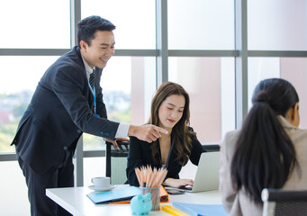 Asian professional successful businessman in formal suit standing showing presenting explaining report investment graph chart data from computer monitor in meeting room to businesswoman colleagues
