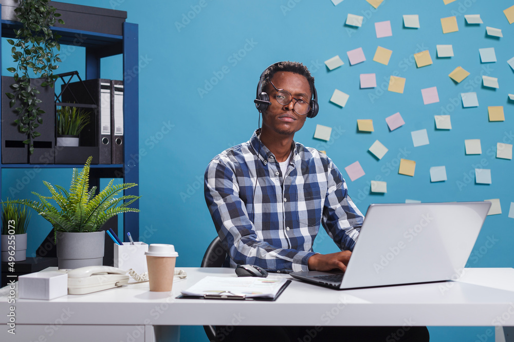 Poster exhausted helpline support operator sitting in call center workspace while looking at camera. fatigu