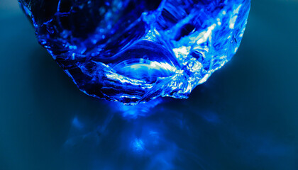 Large shard of blue backlit glass, diamond or topaz, close-up, dark blue background, glass stone, glare.
