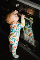 The baby learns to stand near the oven in the kitchen. Little nine months baby boy stands with support at home. Toddler just learnt how to stand on her feet. Baby taking first steps. © Serhii
