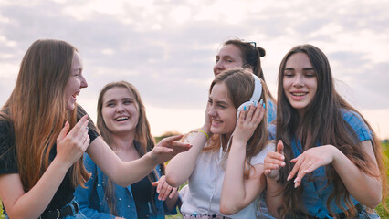 A group of girls of friends are listening to music on headphones and dancing to a friend.