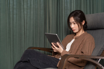 Asian woman holding a tablet is sitting in a rocking chair 