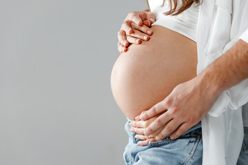 Happy pregnant woman in a studio with husband holding her stomach from behind and wearing bright...