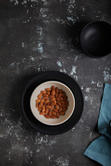 Bowl with almonds on dark rustic concrate textured background. Place for text.