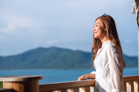 Portrait image of a young asian woman looking at a beautiful sea view from resort terrace