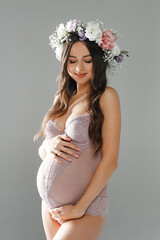 Beautiful smiling pregnant girl in a cute underwear and a wreath of flowers on her head posing in a studio