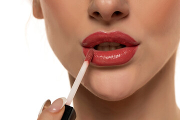 Naklejka premium young beautiful woman apply a lip gloss on her lips on white background