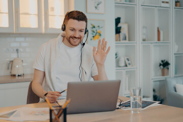 Happy male bearded freelancer sitting in room and having online meeting