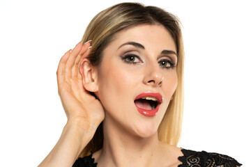 Young blond woman is straining a hand behind her ear while listening on a white background