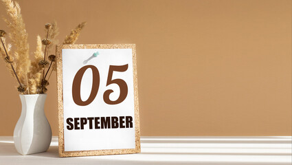 september 5. 5th day of month, calendar date.White vase with dead wood next to cork board with numbers. White-beige background with striped shadow. Concept of day of year, time planner, autumn month