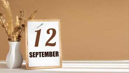 september 12. 12th day of month, calendar date.White vase with dead wood next to cork board with numbers. White-beige background with striped shadow. Concept of day of year, time planner, autumn month